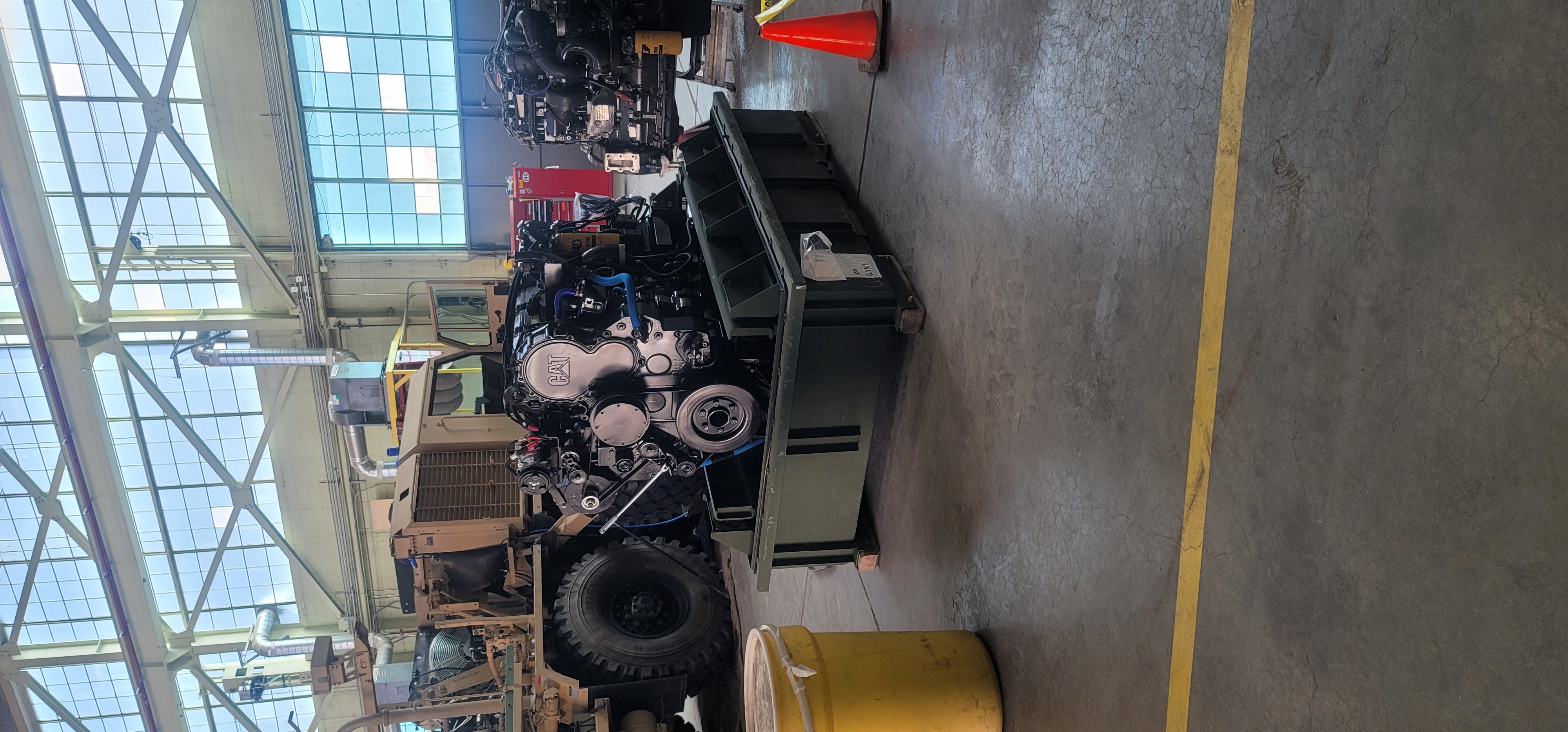 CAT diesel engine on rebuild stand in heavy equipment maintenance bay with military vehicles in background
